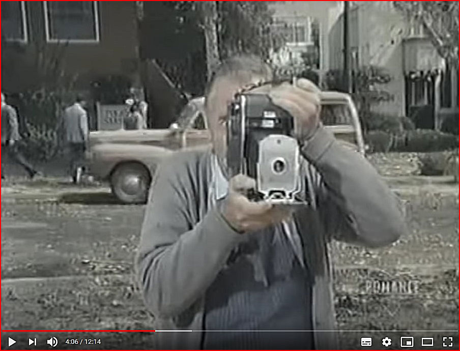 Eli taking a picture with his camera against a backdrop of the newly created Poice Station entrance